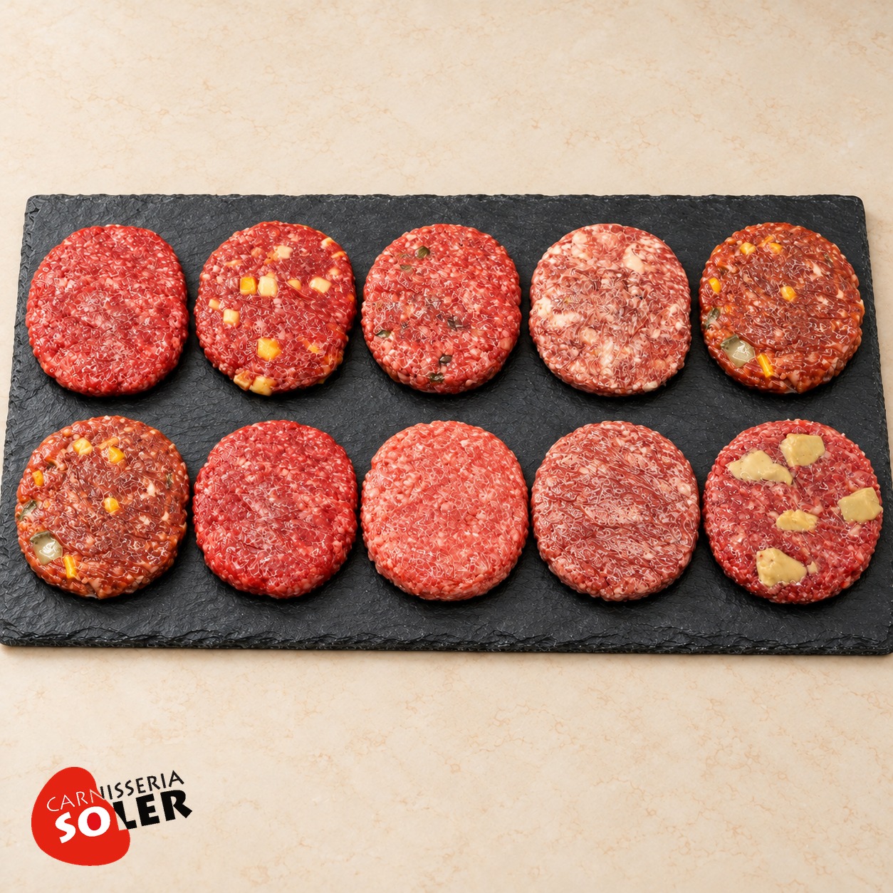 Lot Vedella i Selecció Bovina de Carnisseria Soler, amb 10 hamburgueses crues de receptes diferents sobre pissarra.